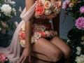 ViktoriiaLu kneeling, wearing a floral bra and skirt made of roses, with a pink sheer scarf, showcasing her tits and ass, surrounded by more roses.