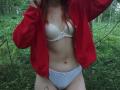 SheritaChieng with red jacket, white bra, and blue panties, showing her tits and pussy in a forest, hands pulling jacket. She has red hair and a tattoo on her thigh.