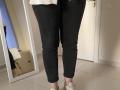 Elliance's black, tight, cuffed jeans and white sneakers, standing with her lower back and butt visible, wearing a white top, in front of a mirror and a door.