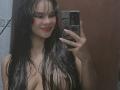 Yurimy with wet black hair, smiling, holding a phone, taking a mirror selfie, showing her bare tits, red lipstick, and white nails. Her nipples are slightly visible.