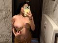Aurora Ferretti, avec ses cheveux noirs et bouclés, porte un soutien-gorge jaune qu'elle a baissé pour montrer ses seins, et elle prend un selfie devant un miroir dans une salle de bain. Elle tient un téléphone jaune..