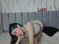 AbbyHillsI is on a bed, wearing white lace lingerie, on all fours, showing her ass and looking at the camera with green and black hair, nose ring, and piercings.