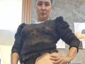 SilverCool69 has a chubby face, wearing a sheer black top with puffed sleeves, showing her small tits and exposed black panties, hand on her belly, in a bathroom.