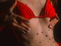 AgataRyili's red bikini top with hands on her chest, adorned with colorful gems on her flat, tan stomach, long white nails, red bikini, and dark background.