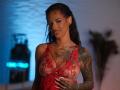 RosaInk in a red lace babydoll, showing tattoos on her right arm and chest, with her hands on her tits, smiling, wearing a silver necklace, and earrings.