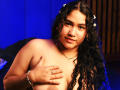 JoyceHill, topless with curly black hair, covering her tits with one hand, wearing a star hairpiece, necklace, and ring, against a blue-lit background, smiling softly.