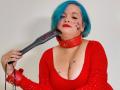 LeidiBlue with blue hair, red lipstick, and red top, holding a black dildo with "DOZO" in red, wearing a red leather collar, and a star tattoo on her chest.