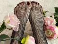 MiraRosse's feet in black fishnet stockings, with pink roses around them. Her toenails are painted dark red. She's lying on a white, fluffy surface.