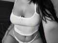 Olieri's white ribbed tank top, showing her big tits, with a small bow, and white panties, sitting with her dark hair on the right, wearing a watch.