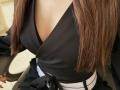 Kattina's black v-neck top, showing her big tits, with long brown hair covering the right side, a black jacket on her left, and a white belt around her waist.