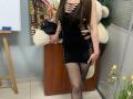 Omella wearing a black, cut-out dress with her tits slightly visible, black fishnet stockings, and a white teddy bear behind her. Her long brown hair covers her face.