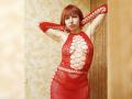 LaylaHottyX with red lace dress, arms raised, showing her tits through cutouts, red fishnet sleeves, red hair, pale skin, in a sexy, confident pose, in a warm room.