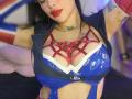 Kkole with big, shiny blue tits, wearing red strappy lingerie, a denim vest, and pink gloves, has red lipstick and a green butterfly necklace, in a selfie.