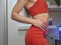 Side view of MilaYanis, wearing a tight red crop top and matching skirt, highlighting her toned abs and curvy hips. Long blonde hair, slender fingers on her waist. Fucking sexy.