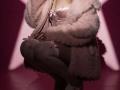 Destinis is squatting, wearing a pink satin bra, fluffy pink coat, white thigh-highs with pink bows, and pink heels. Boobs are visible, coat partially open.