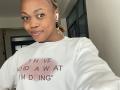 Sashie with light brown skin, small nose ring, braided hair, white sweatshirt, and earbuds, smiling at camera, brown eyes, white teeth, soft expression, Sashie's tits not visible.