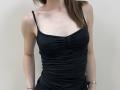 Ramilla wearing a black, ruched, spaghetti-strap dress, showing her tits and slim arms, with brown hair, a gold watch on her right wrist, and a bracelet.