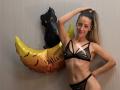 ViktoriiaLu trägt schwarze Spitzendessous, die ihre Brüste und Vulva zeigen, hat einen hohen Pferdeschwanz, lächelt und steht neben einem Halloween-Mondballon mit Fledermäusen und der Aufschrift "Frohes Halloween".".