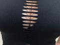 Tilliana's black top has horizontal slit patterns running down the center, revealing her large, tan-skinned boobs. The slits expose her nipples and a bit of her black bra.