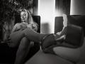 VeraNoires, nude with tits, sits in a chair, legs crossed, wearing heels, looking at camera, black and white, indoor, potted plant in background, confident smile, soft lighting.