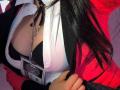 KiraBerry's red jacket is open, revealing her black bra and white shirt. Her hand is gripping the jacket. A chain with a pendant hangs over her tits.