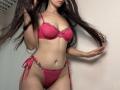 Tisia with long dark hair, wearing a pink lace bra and matching thong with floral accents, holding her hair, showing her small, perky tits and slim, flat-stomached pussy.