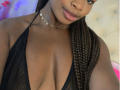 VenusWilly with dark skin, braided hair, and full lips, wearing a black mesh halter top that shows her big, shiny tits. She's also wearing a silver choker.