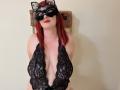 MelanieFrancaise with red hair, black lace bodysuit, deep cleavage, large tits, black mask with cat ears, red lipstick, arms behind back, standing in front of a rope.