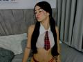 KarinaCurvy with long black pigtails, wearing a sheer white crop top with a red plaid tie, showing small tits and a red thong, eyes closed, pouty lips, tattoo on left arm.
