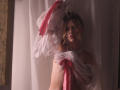 RosaVance with wavy blonde hair, crown, white and pink sheer fabric draped over tits and arms, pearl necklace, looking sad, soft lighting, vintage wallpaper on left.