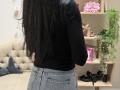 Dalaila with long black hair, wearing a black long-sleeve top and blue jeans, standing with her back to the camera, showing her ass and jeans pockets.