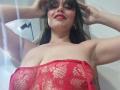 MadissonFontaine with red lace mesh top, showing big tits, smiling with red lipstick, hands in dark hair, wearing hoop earrings, in a low-angle shot.