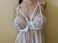 Tisia's boobs are covered in a sheer white lace babydoll with floral patterns, and she's wearing a delicate chain necklace that drapes over her chest.