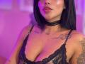 MajoJones with black lace bra, shiny skin, tattoos on chest and shoulder, choker, pink-purple light, lips slightly parted, showing cleavage, dark straight hair, subtle makeup, sexy.