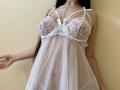 Tisia wearing a white lace babydoll with straps and a small bow, exposing her big tits through sheer fabric. Her long brown hair falls over her shoulders.