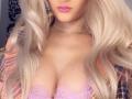 MademoiselleBella has blonde hair, pink lipstick, and a gold necklace. She's wearing a pink lace bra, showing her big tits, with a plaid shirt open.