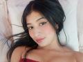NaiaSanders has dark long hair, brown eyes, and pink lipstick. She's lying on a pillow, wearing a red strapless top, with a cute nose piercing. Her tits are slightly visible.