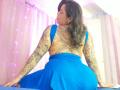 Chili with tattoos on her back and arms, wearing a blue dress, sitting with her ass up, looking over her shoulder. Her brown hair is wavy, and she's looking sexy.