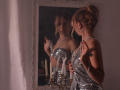 RosaVance in a sparkly silver dress, reflecting in a mirror, holding her tits, wearing a necklace, standing next to white candles, her ass slightly visible.