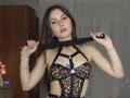 KimberlyZampieri with long brown hair, wearing a leopard print harness with black straps, holding a black strap in front of her tits, looking at the camera.