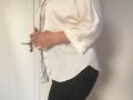 Elliance's white silk shirt, slightly open, reveals a hint of her tits. She's holding a door handle, wearing black pants, her right hand showing a ring.