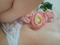 AmeliaMaiv's pale, soft skin with a small belly button, wearing white lace panties, has pink and yellow roses resting on her lower belly.
