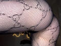 Close-up of DeeannMilloy's curvy buttocks covered in black fishnet stockings with a floral pattern. Yellow light glows beneath the fishnets, creating a provocative and erotic vibe.