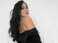 JessyBarnnett with long black hair, looking over her shoulder, wearing a black off-shoulder top, exposing her back and a hint of her tits. She has a subtle smile.