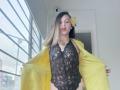 ArianaBlonde with blonde hair, wearing a black lace bodysuit, yellow jacket open, yellow flower in hair, showing her tits and pussy through lace, standing by a window.