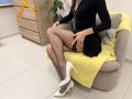 Rorria est assise sur une chaise, vêtue d'une robe noire, de bas résille et de talons blancs, sa main posée sur sa jarretière en dentelle noire, avec une couverture jaune et un jouet bleu..