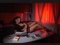 AmelieReea with big tits, black crop top, red plaid skirt, black heels, lying on kitchen counter, reading book, red curtains, books, and cards scattered around, red lighting.