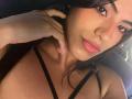 EvaGate with dark hair, pink lips, and brown eyes, wearing a black strappy top, touching her neck with a hand, showing a cute, sexy face.