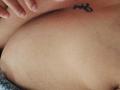 MirandaDreams' bare chest with a small tattoo of a butterfly near her right nipple, her hand resting above it. Boobs, tan skin, slight texture visible.