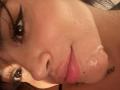MajoJones's face with cum on her lower lip and chin, dark eyebrows, and a tattoo visible near her neck. She has a slight pout and her lips are parted.